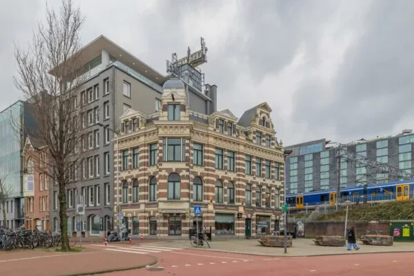 Historisch pand aan de De Ruijterkade in Amsterdam met een passerende trein op de achtergrond.